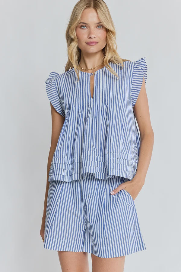 A woman modeling a matching blue and white striped two-piece set consisting of a ruffled sleeveless top with a keyhole neckline and pleated peplum hem, paired with matching striped shorts, against a light gray studio background.