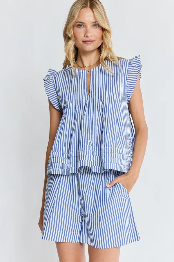 A woman modeling a matching blue and white striped two-piece set consisting of a ruffled sleeveless top with a keyhole neckline and pleated peplum hem, paired with matching striped shorts, against a light gray studio background.